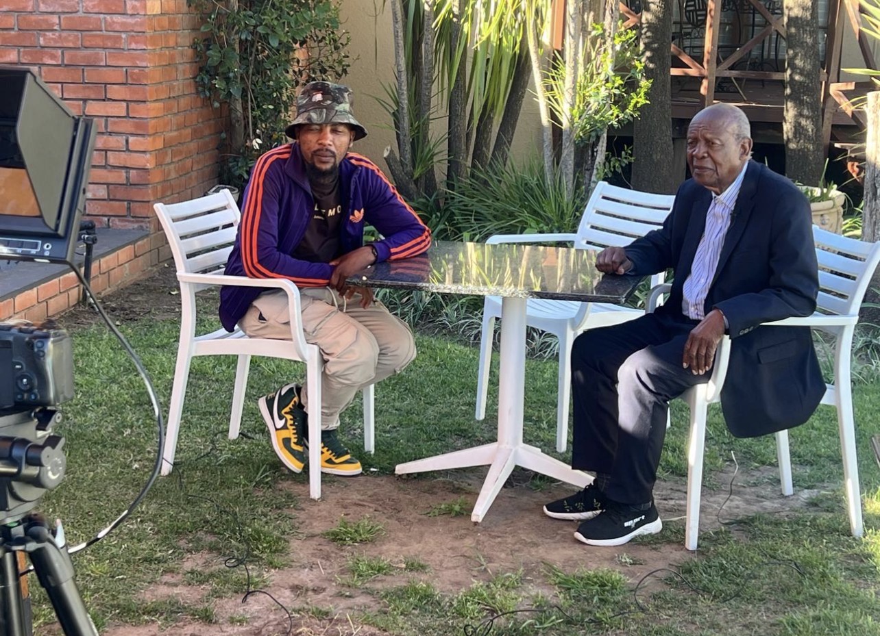 A BMC interview in progress: two people seated at a garden table with a camera and teleprompter